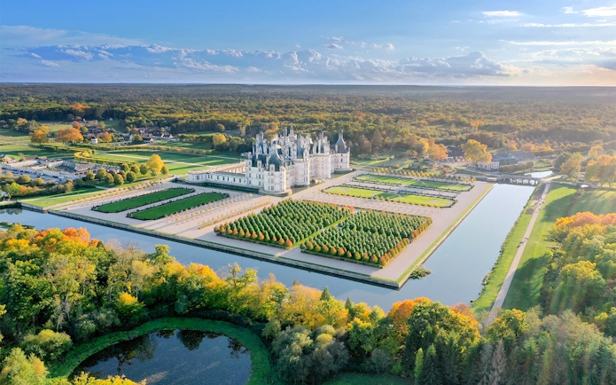 Chambord Castle and gardens aerial view, showcasing symmetrical landscaping and surrounding forest.