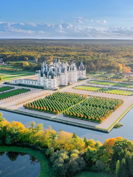 Chambord Castle and gardens aerial view, showcasing symmetrical landscaping and surrounding forest.