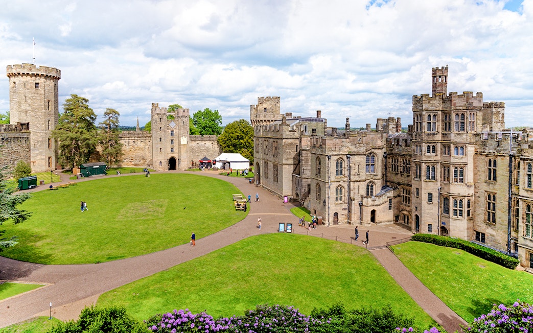 Warwick Castle courtyard with historic stone buildings and lush green lawn.