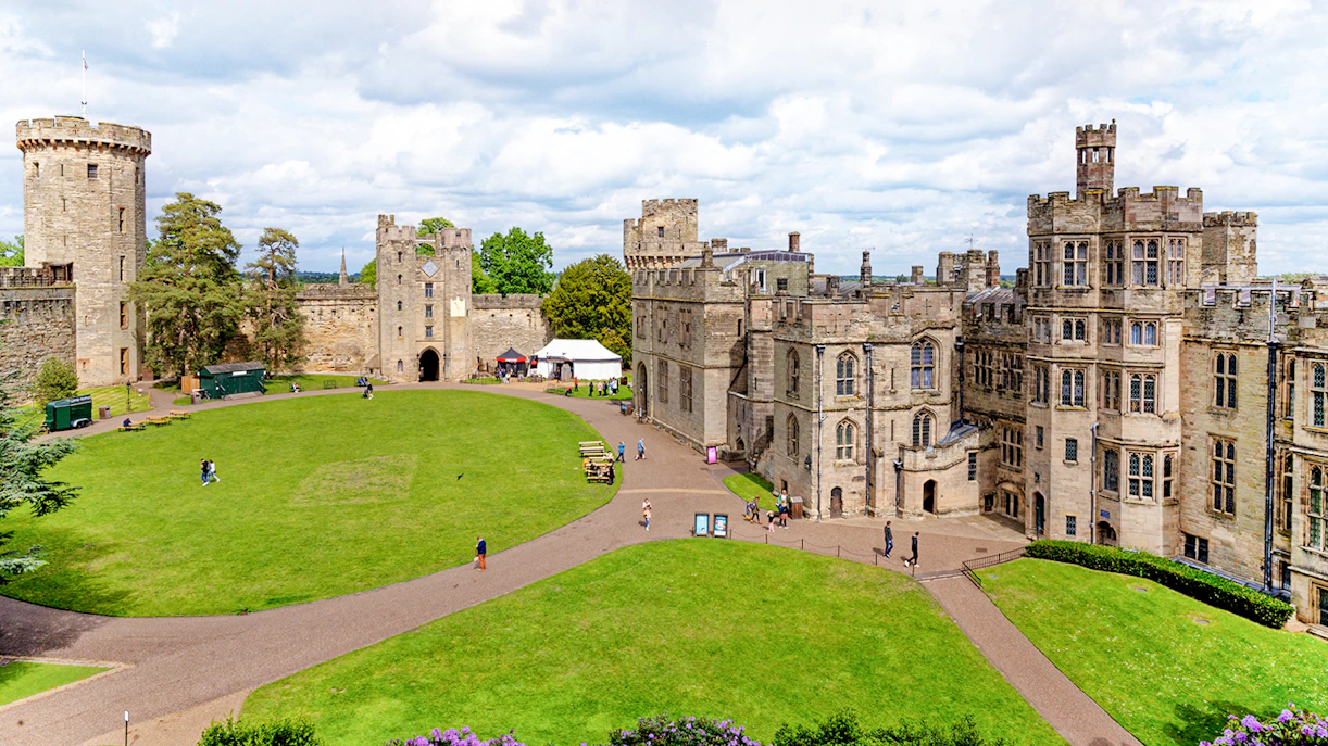 Warwick Castle courtyard with historic stone buildings and lush green lawn.