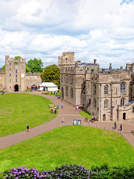 Warwick Castle courtyard with historic stone buildings and lush green lawn.