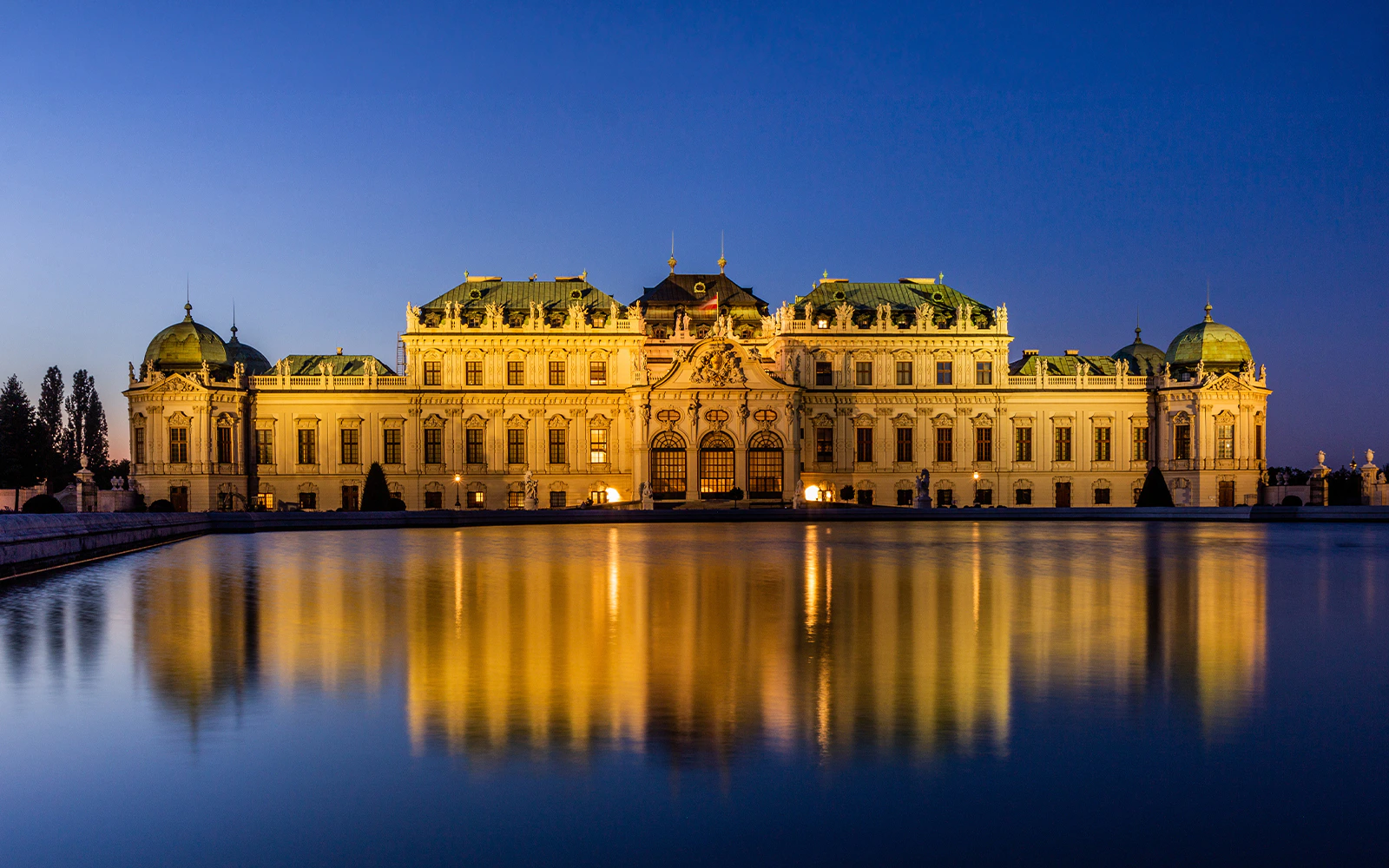Upper Belvedere palace illuminated at dusk, reflecting in the water, Vienna, Austria.