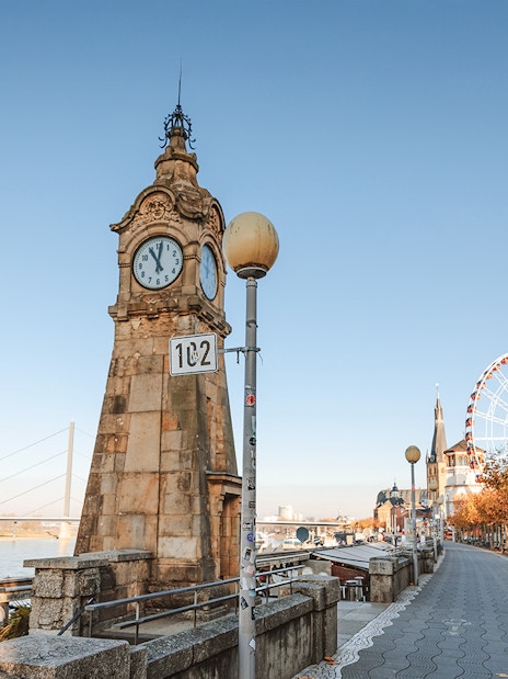 Clock tower and promenade in Dusseldorf Old Town with Ferris wheel in the background.