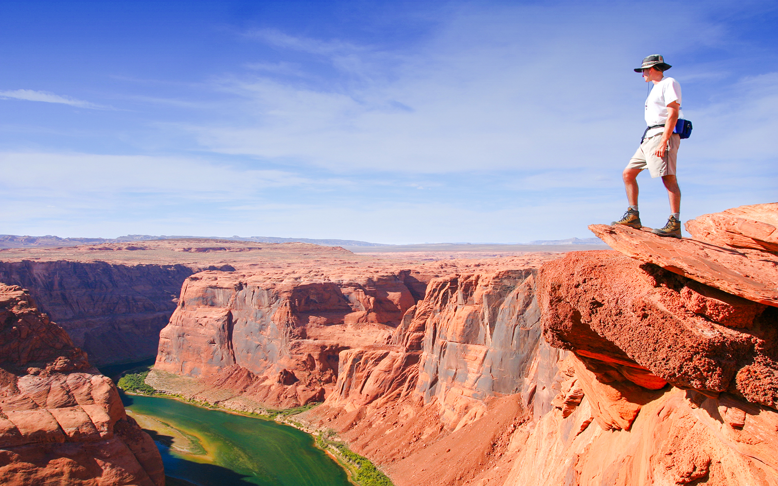 Hiker standing on a cliff edge overlooking the Grand Canyon.