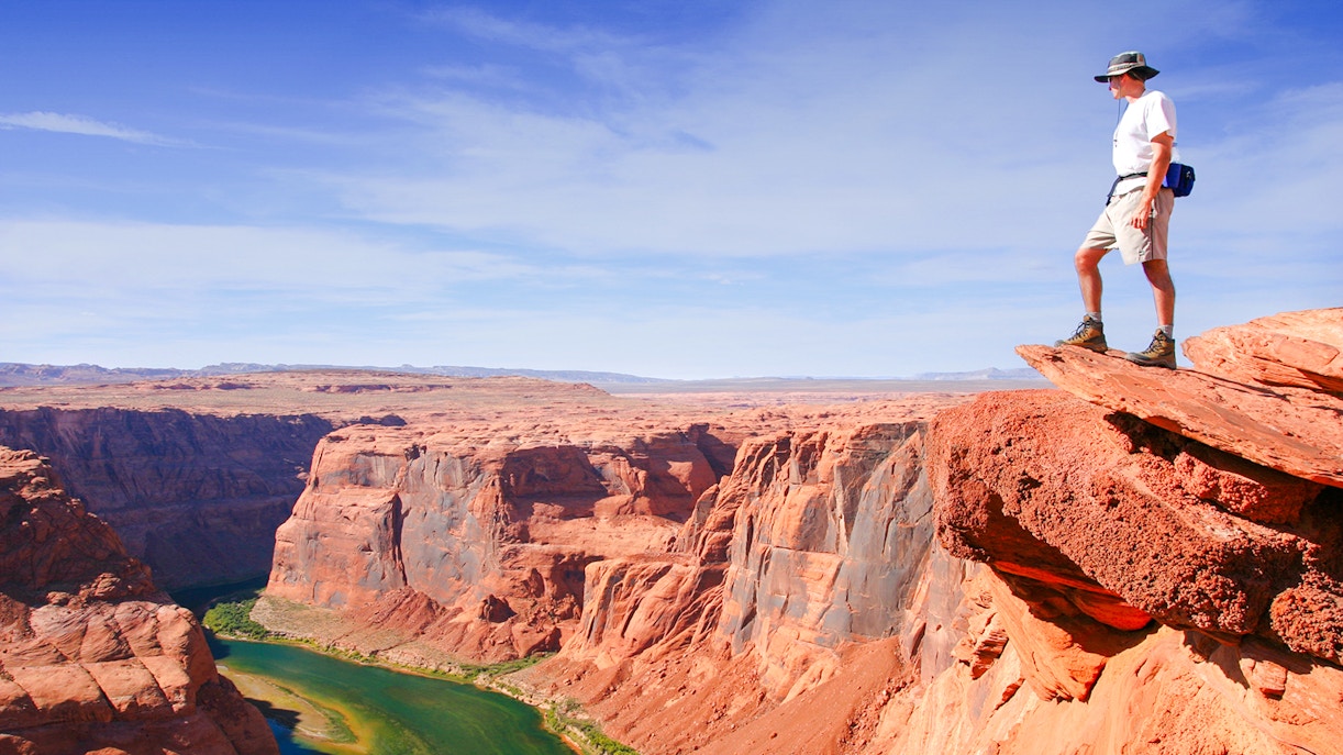Hiker standing on a cliff edge overlooking the Grand Canyon.