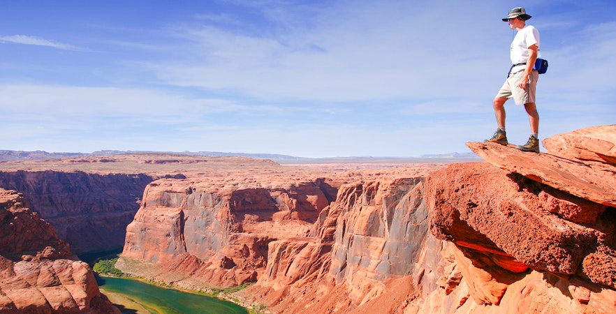 Hiker standing on a cliff edge overlooking the Grand Canyon.