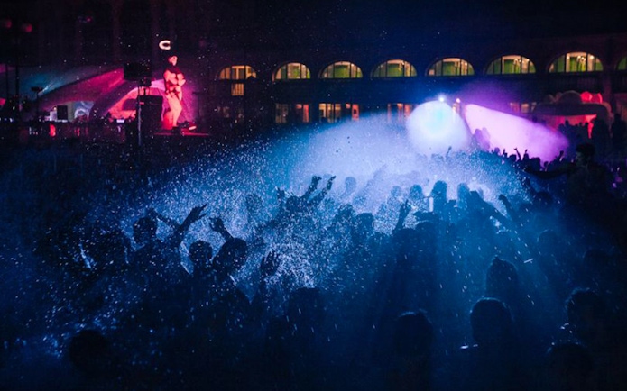 Crowd enjoying a vibrant night concert with colorful lights and water effects.