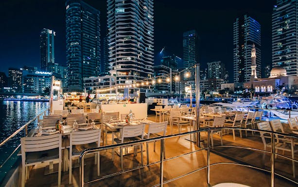 Seating area on Alexandra Sea Lounge Dhow Cruise with city skyline at night.