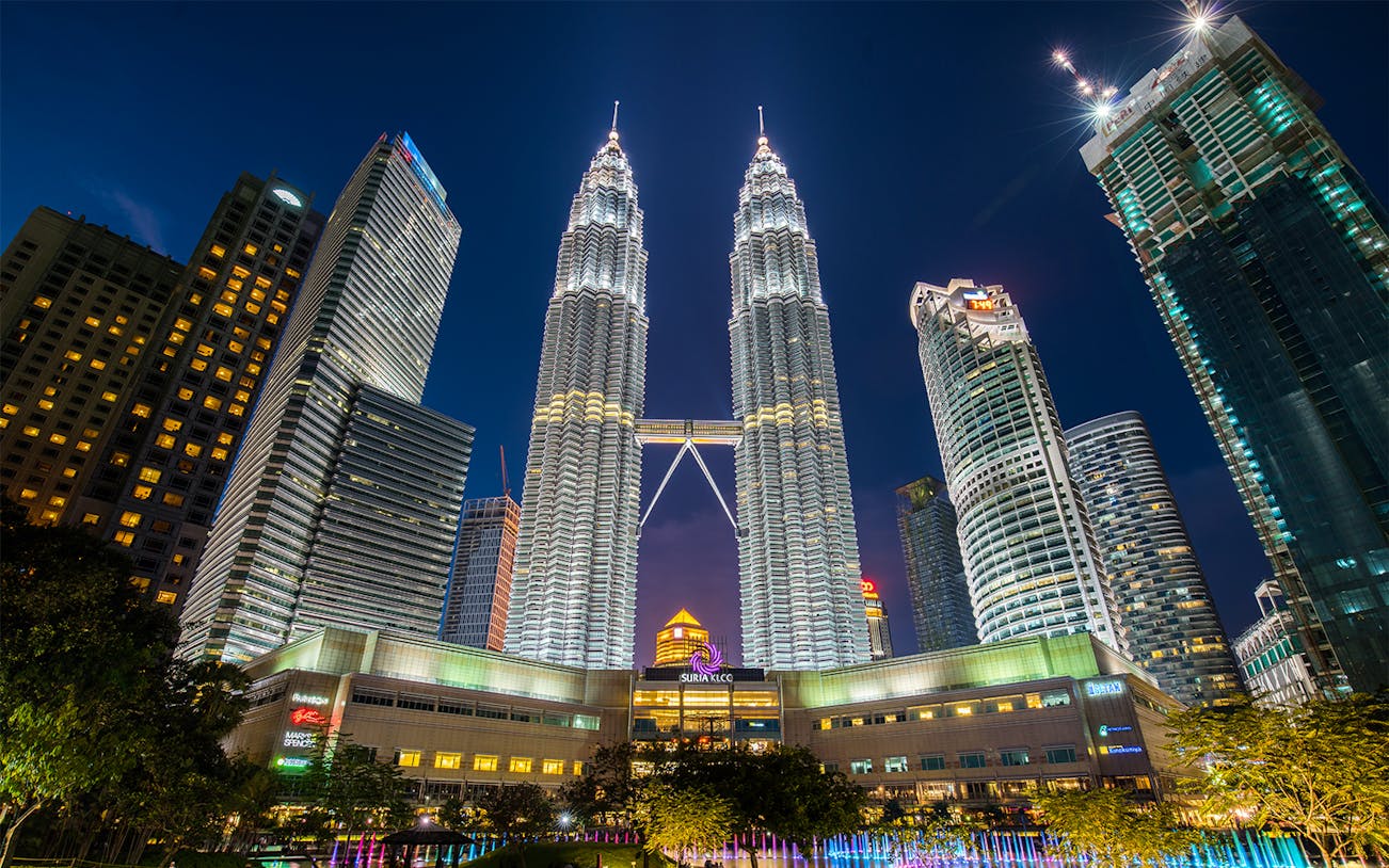 Petronas Twin Towers illuminated at night in Kuala Lumpur, surrounded by city skyscrapers.