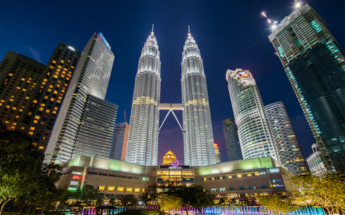 Petronas Twin Towers illuminated at night in Kuala Lumpur, surrounded by city skyscrapers.