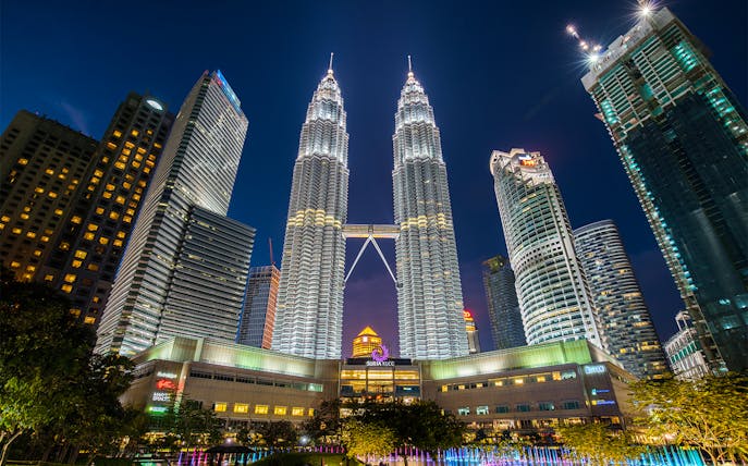 Petronas Twin Towers illuminated at night in Kuala Lumpur, surrounded by city skyscrapers.