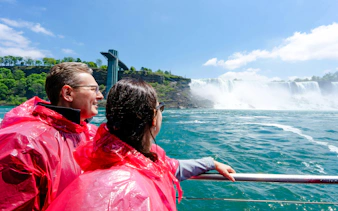 Tourists in red ponchos on a boat near Niagara Falls with observation tower in view.