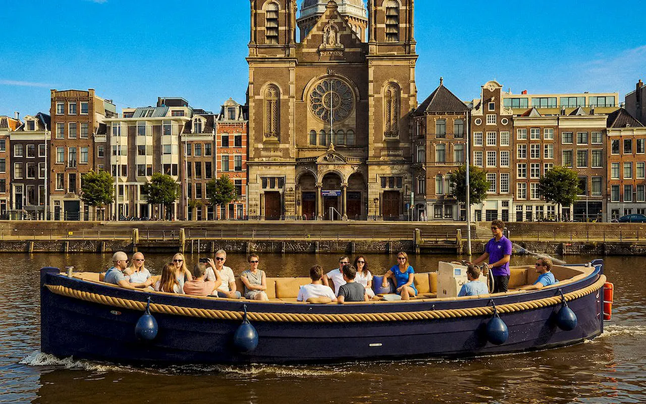 Open boat with tourists cruising Amsterdam canal near historic church.