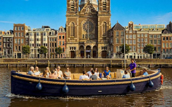 Open boat with tourists cruising Amsterdam canal near historic church.
