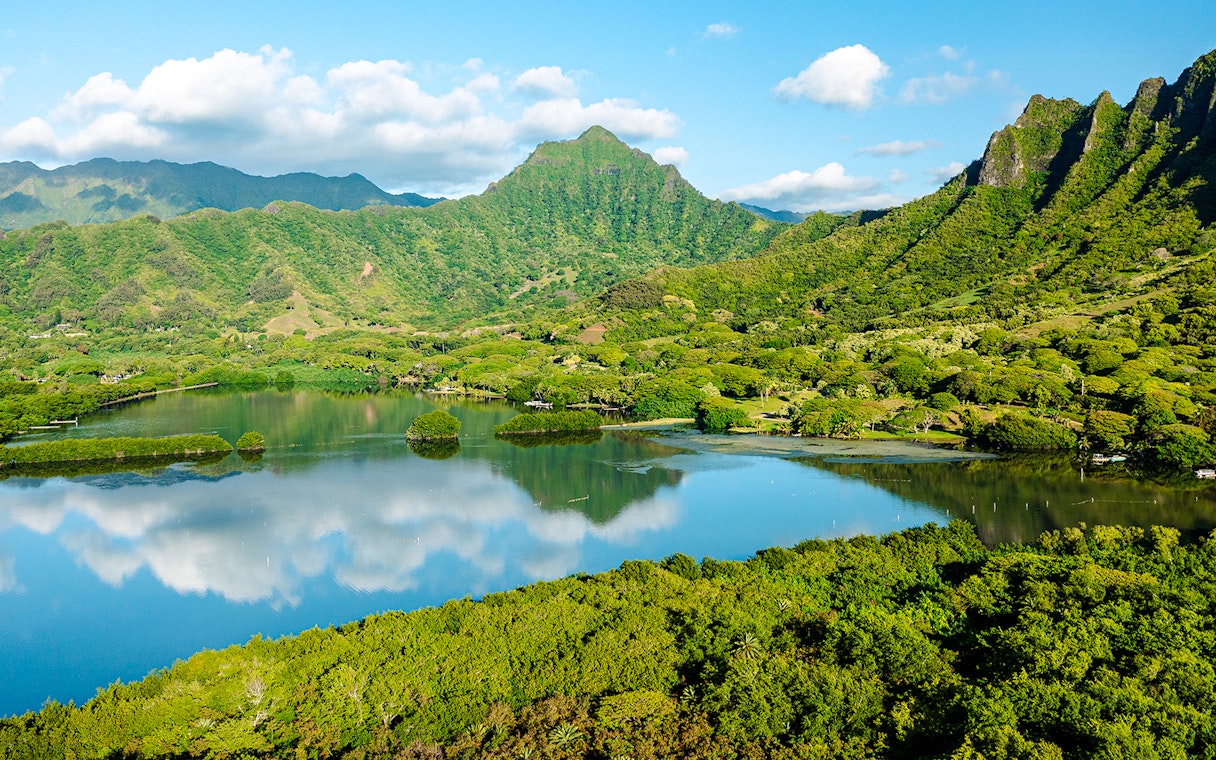 Lush green mountains and a reflective lake at Kualoa Ranch, Hawaii.