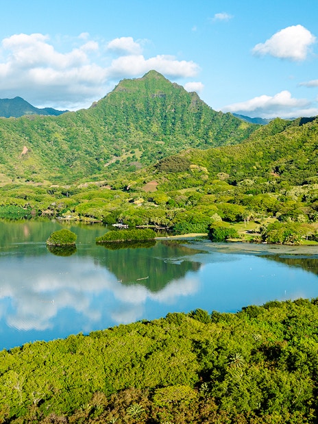 Lush green mountains and a reflective lake at Kualoa Ranch, Hawaii.