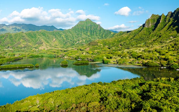 Lush green mountains and a reflective lake at Kualoa Ranch, Hawaii.