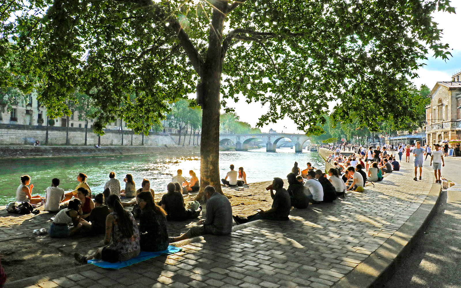 People relaxing by the Seine River at Paris Plages, with a bridge in the background.