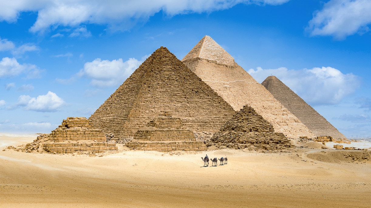 Pyramids of Giza with camels in the foreground under a blue sky.