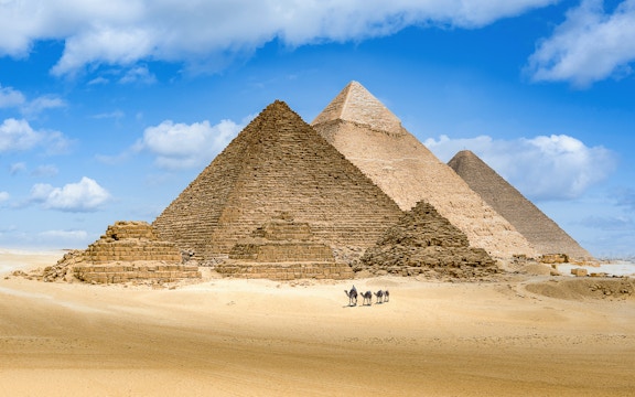 Pyramids of Giza with camels in the foreground under a blue sky.