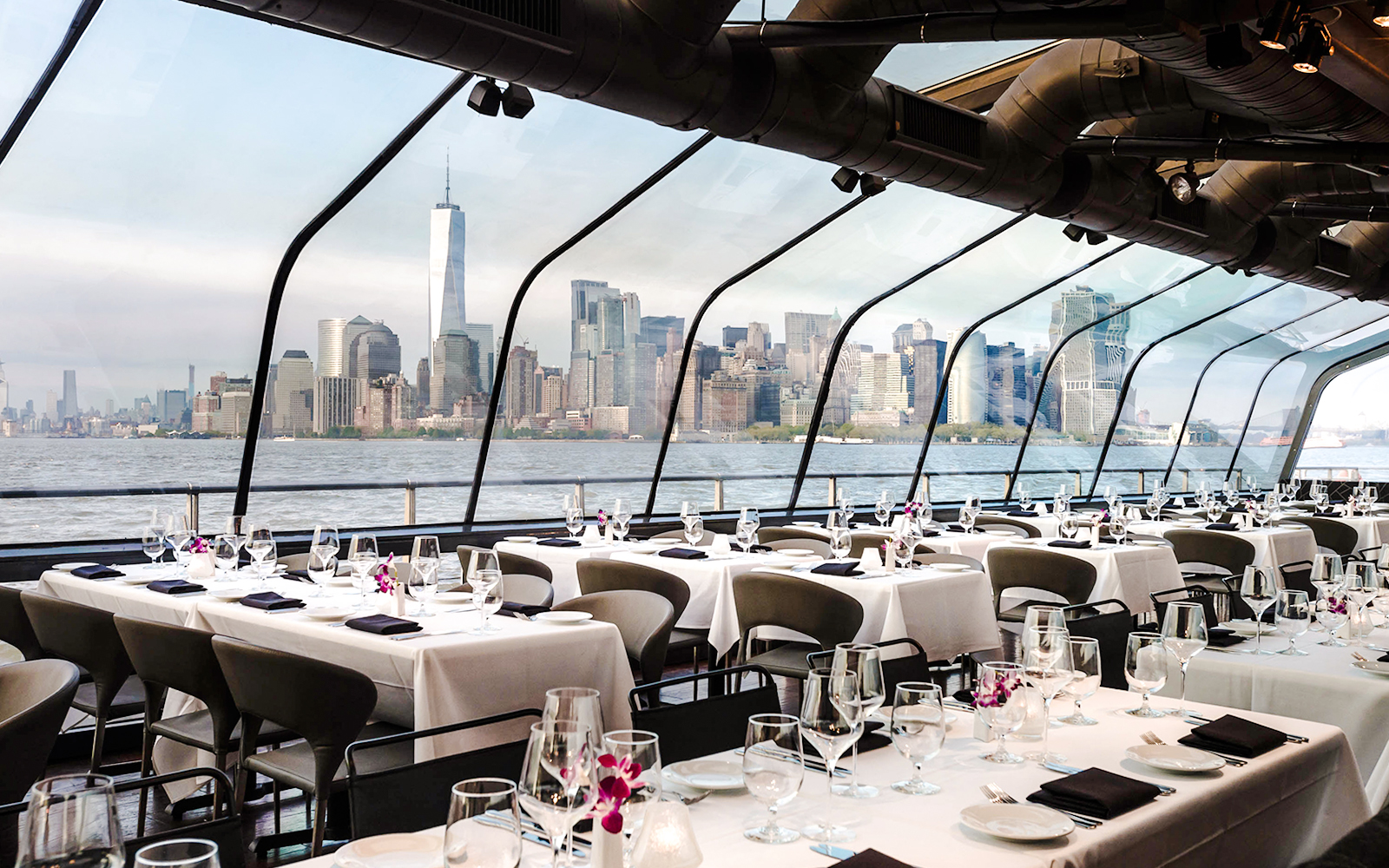 Glass-enclosed dining area on a luxury boat with New York City skyline view.