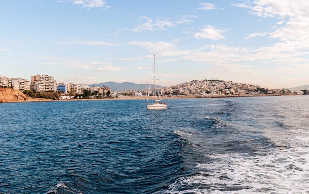 Sailboat on the water with Piraeus cityscape in the background, Athens, Greece.