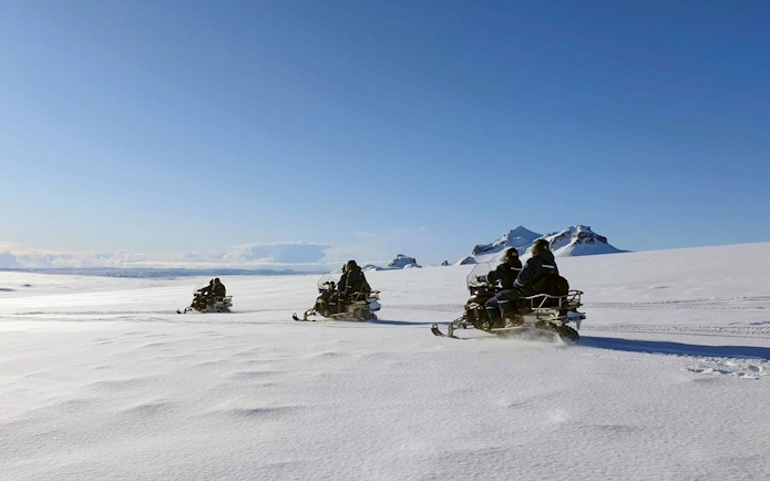 Snowmobilers riding across a glacier during Secret Lagoon hot spring tour in Iceland.
