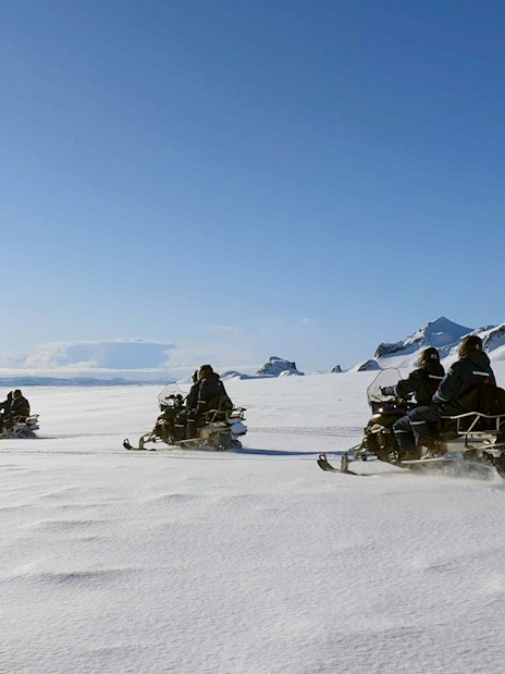 Snowmobilers riding across a glacier during Secret Lagoon hot spring tour in Iceland.