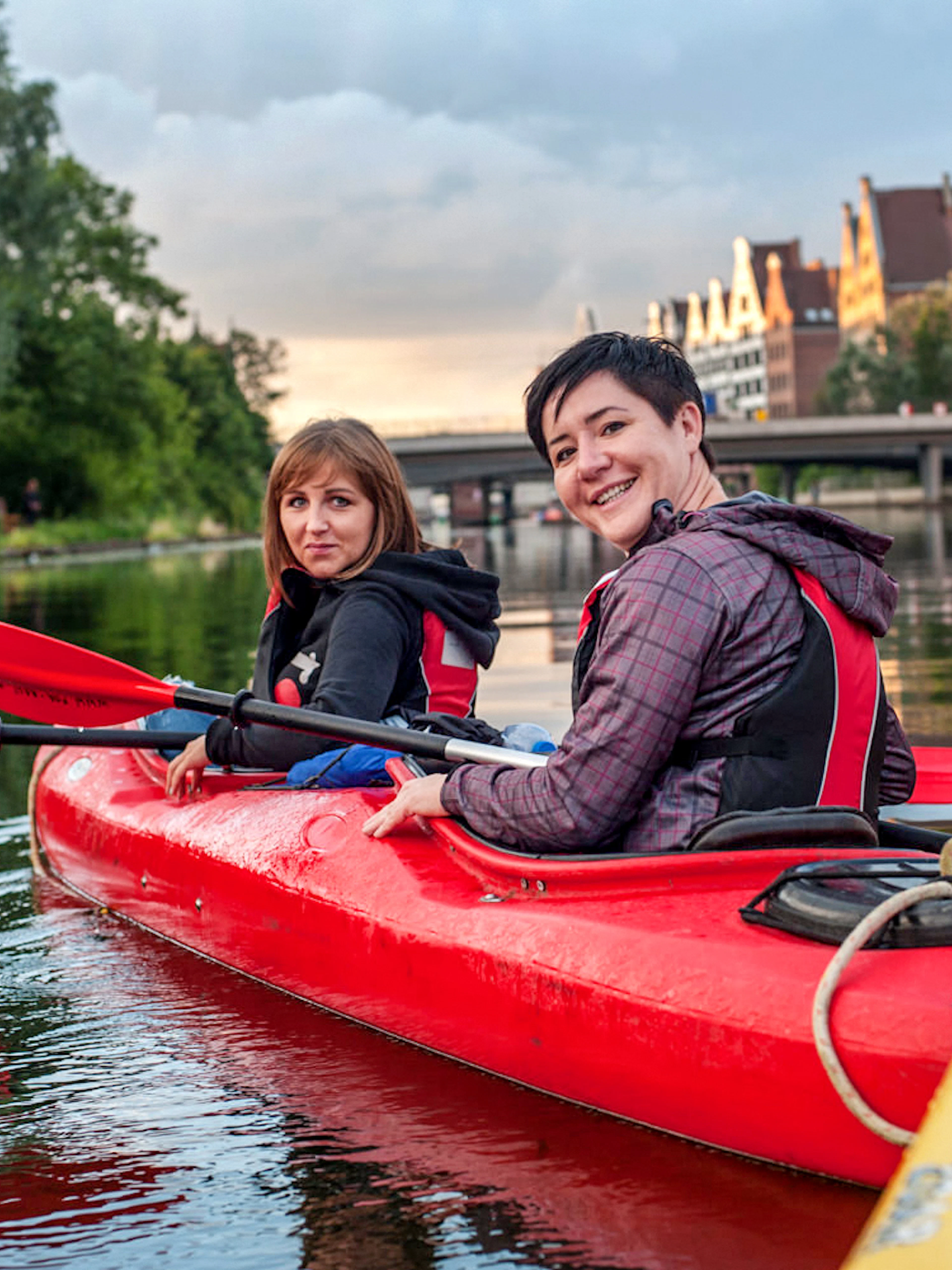 Kayakers paddling on a river in Gdansk with historic buildings in the background.