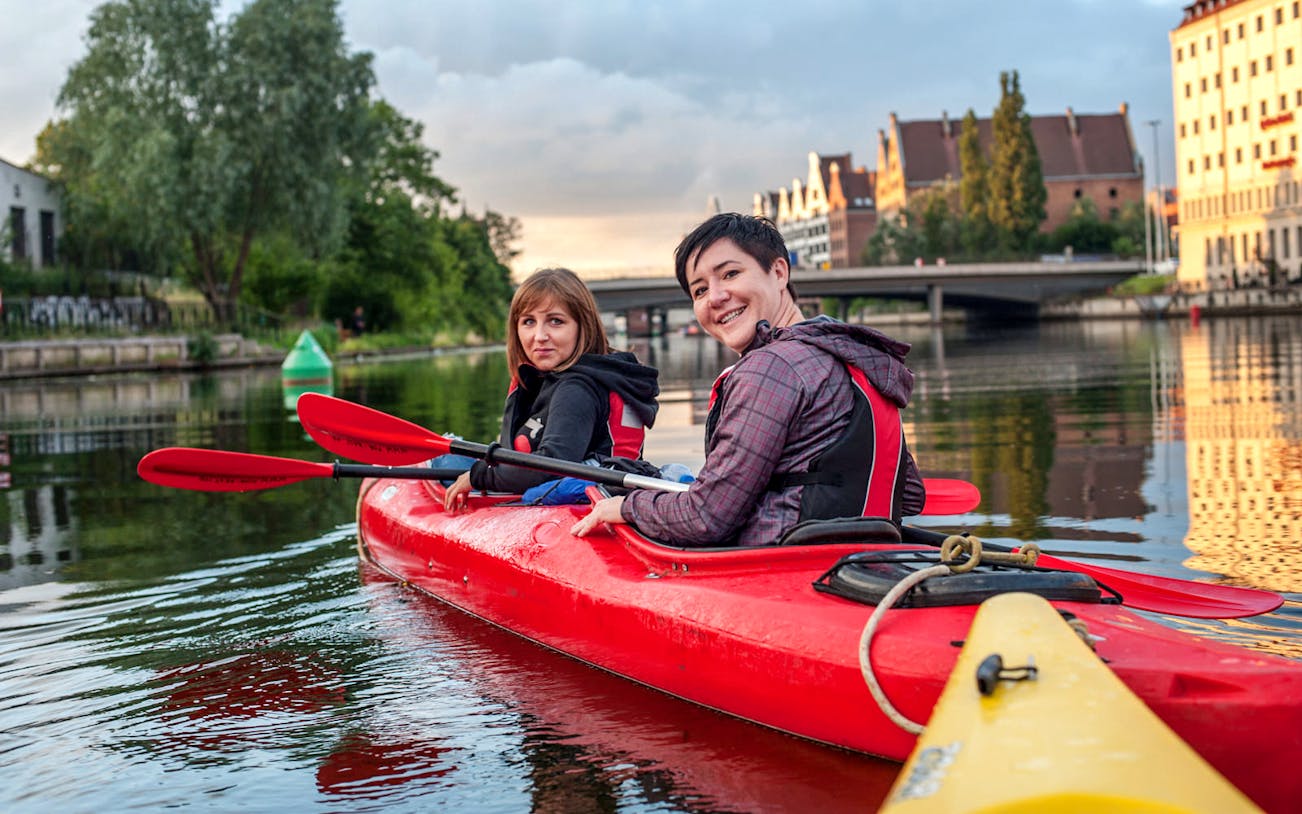 Kayakers paddling on a river in Gdansk with historic buildings in the background.