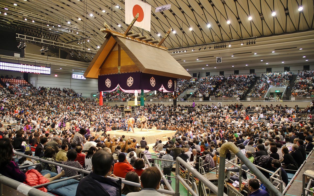 Sumo wrestlers competing in a packed Tokyo arena under a traditional Japanese roof.