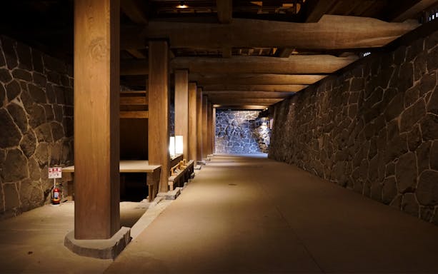 Interior stone corridor of Kumamoto Castle, featuring wooden beams and dim lighting.