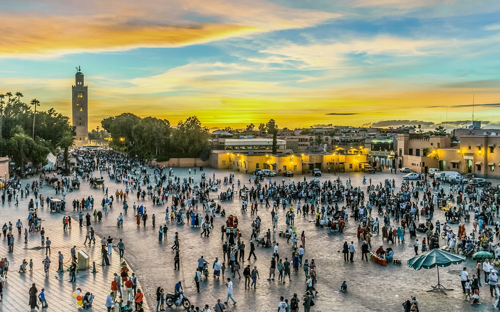 Tourists exploring the vibrant Jamaa el Fna market in Marrakech, Morocco, with traditional Moroccan stalls and local crowd