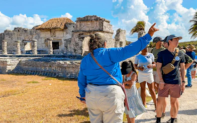 Tour guide explaining Tulum stone temple and ruins to tourists.