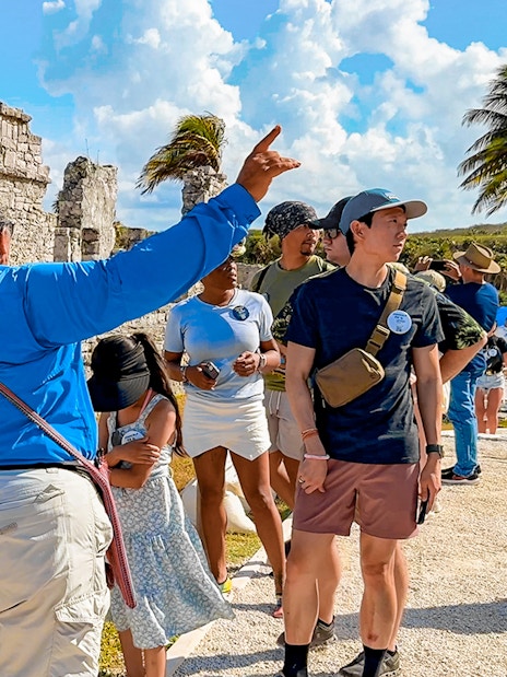 Tour guide explaining Tulum stone temple and ruins to tourists.