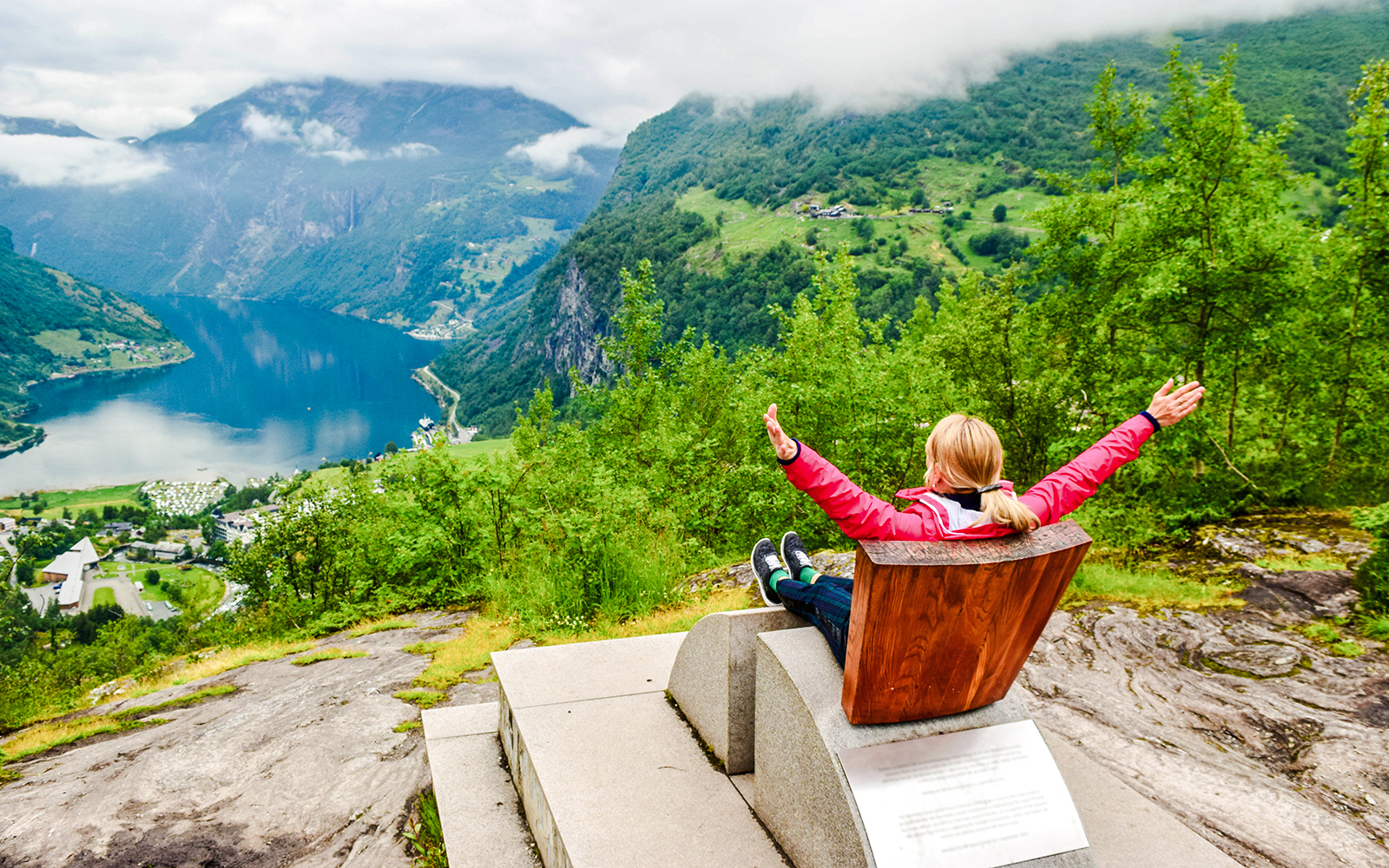 Tourist enjoying view at Flydalsjuvet Viewpoint, Geiranger, overlooking fjord and mountains.