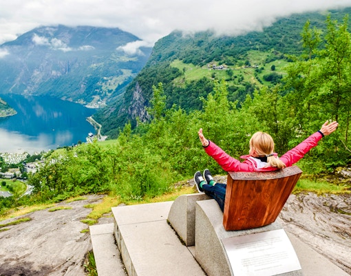 Tourist enjoying view at Flydalsjuvet Viewpoint, Geiranger, overlooking fjord and mountains.