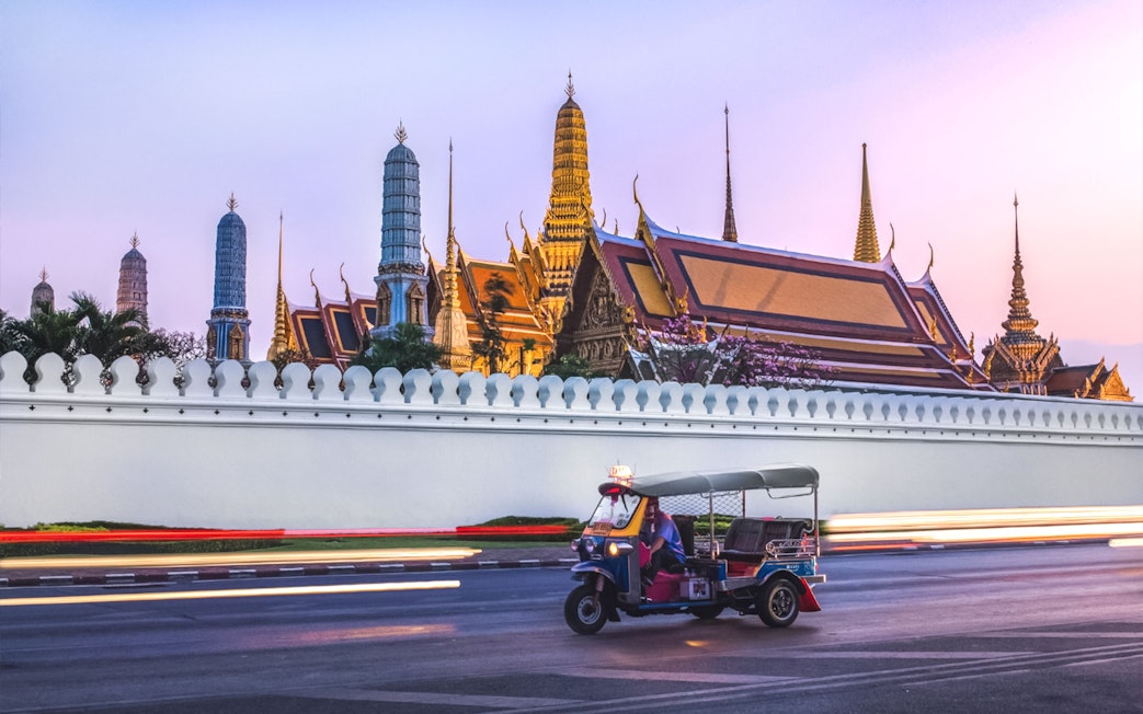 Tuk-tuk driving past Wat Phra Kaew in Bangkok at sunset.