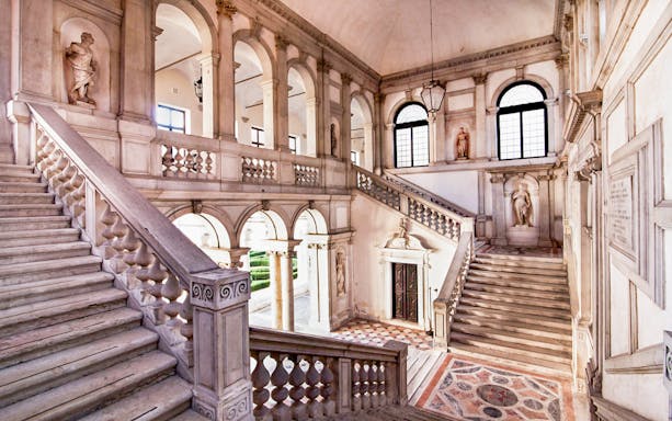 Staircase inside Giorgio Cini Foundation, Venice, with classical statues and arches.