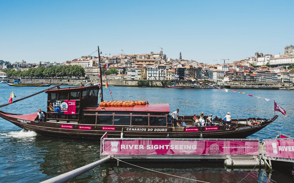 Tourists boarding a sightseeing boat at Douro Pier, Porto, with cityscape in the background.