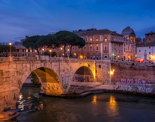 Trastevere bridge and buildings at dusk during a guided tour in Rome.