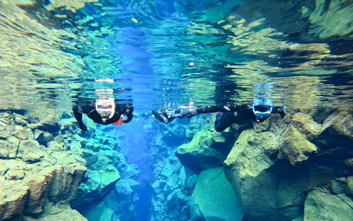 Snorkelers exploring the clear waters and rocky formations of Silfra in Iceland.