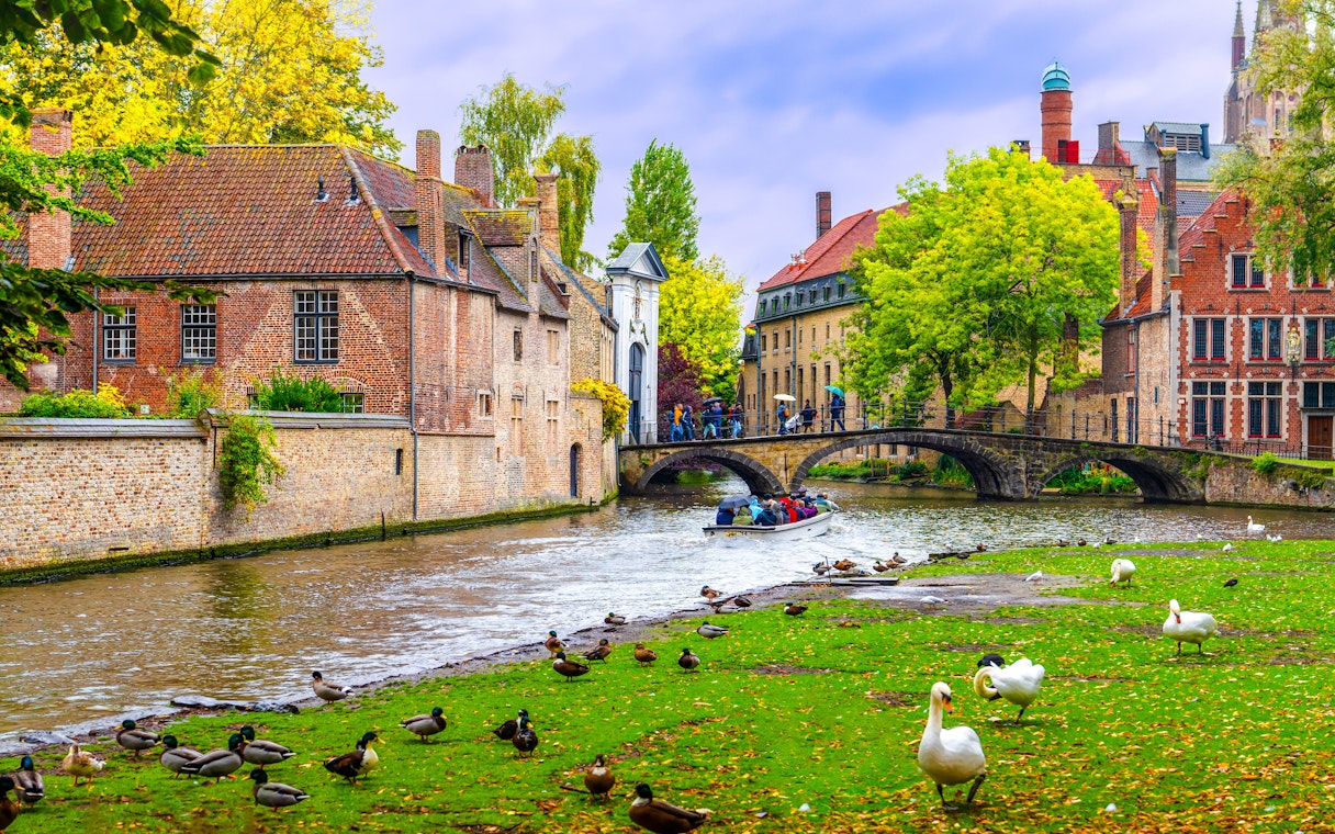 Stone bridge over Lake of Love with swans and tourists, near Begijnhof, Bruges, Belgium.