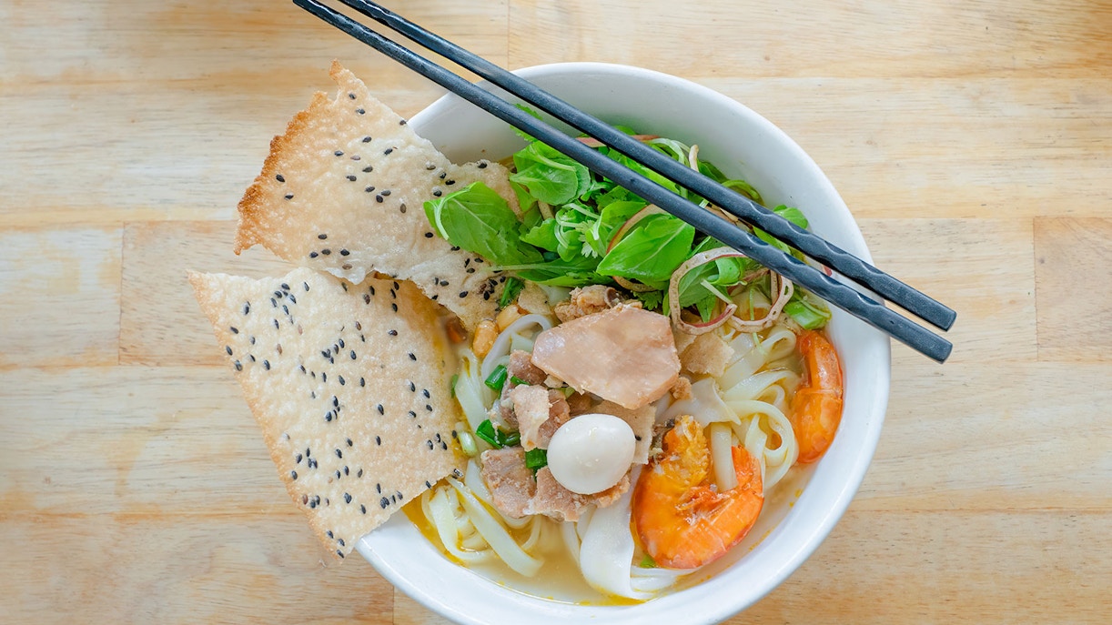 Vietnamese rice noodles with shrimp, herbs, and sesame crackers in a bowl.