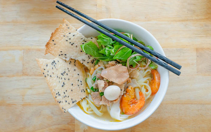 Vietnamese rice noodles with shrimp, herbs, and sesame crackers in a bowl.