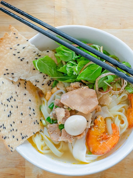 Vietnamese rice noodles with shrimp, herbs, and sesame crackers in a bowl.