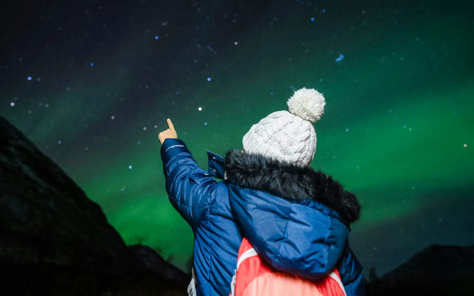 Person pointing at Northern Lights in Tromsø sky during aurora chase.