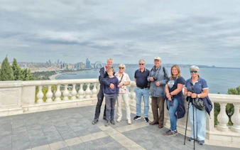 Group of tourists on a guided walking tour overlooking Baku cityscape and Caspian Sea.