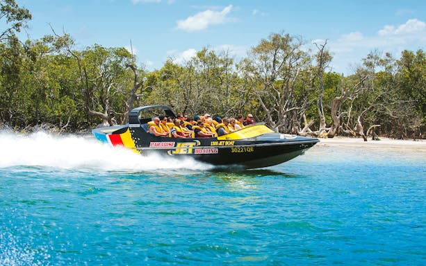 Jet boat with passengers speeding on water near lush shoreline, part of Aquaduck and Paradise Jet Boating combo.