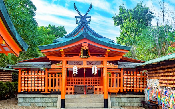 Shinto shrine in Sagano, Kyoto, with vibrant orange architecture and surrounding greenery.